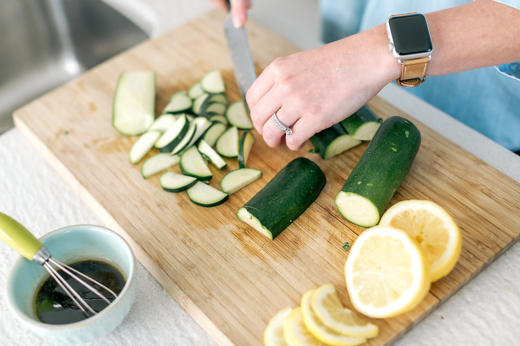 Slicing fresh zucchini on a cutting board with lemon and a small bowl of dressing — building balanced, blood sugar-friendly meals