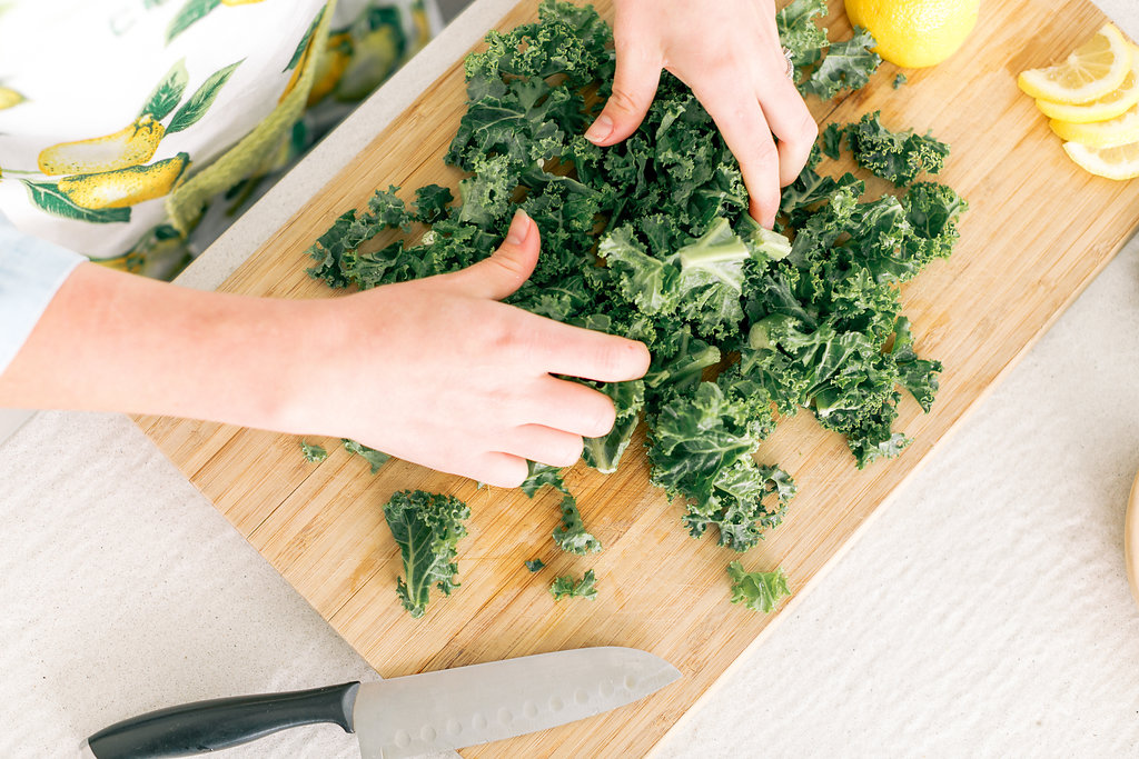 Hands tearing fresh kale on a wooden cutting board with sliced lemon — preparing blood sugar-friendly meals for a gestational diabetes diet plan